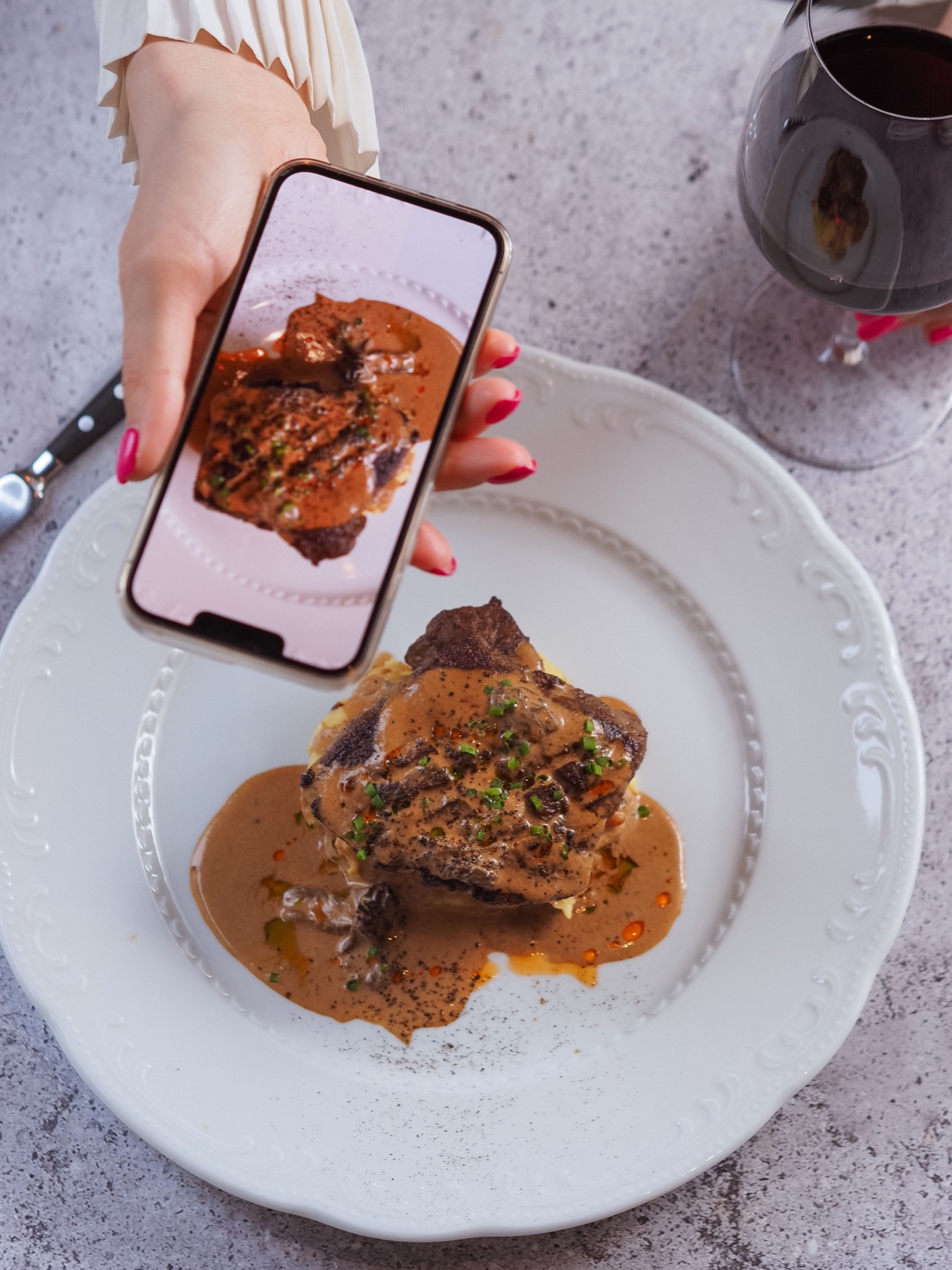 A hand holding a phone above a plated steak